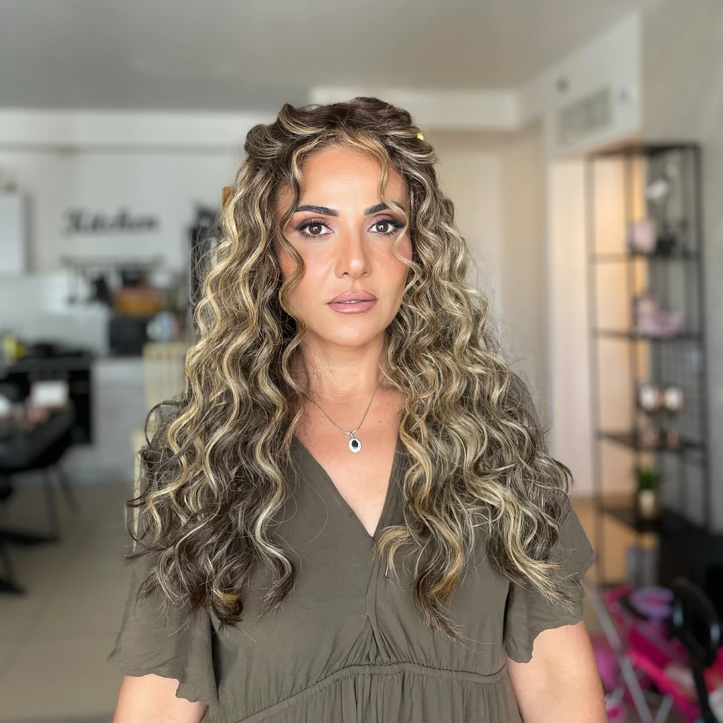 אישה עם איפור גלאם ושיער מתולתל עם גוונים בהירים